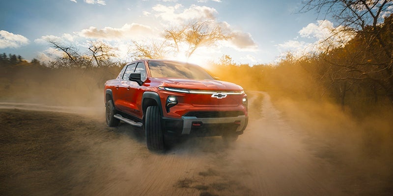 Red pickup truck driving on a dusty road at sunset